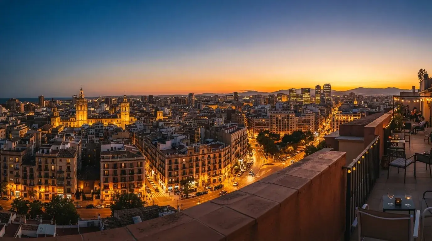 Vista panorámica de una ciudad española al atardecer con edificios iluminados y un cielo anaranjado.